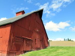 A red barn on a green lawn under a blue sky in Idaho.